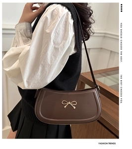 Detail shot of a dark brown faux leather shoulder bag with a gold bow metal ornament