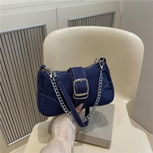 Blue denim crossbody bag with large silver buckle and chain strap on a beige chair