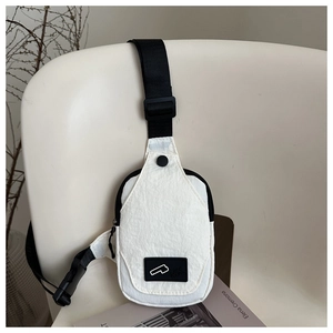 Close-up of a white minimalist canvas chest bag with black adjustable strap on a chair