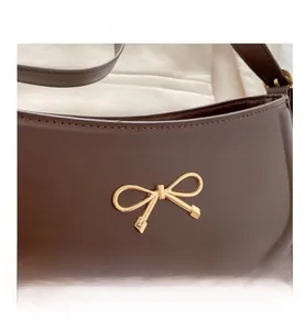 Close-up of a dark brown leather bag featuring a polished gold metal bow decoration