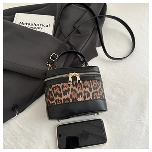 Close-up of leopard print cylinder handbag with gold hardware and bottom metal studs