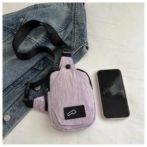 Close-up of light purple nylon chest bag on denim jacket with buckled strap and MX logo