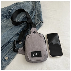 Close-up of gray nylon crossbody bag with adjustable black strap and buckle on white bed