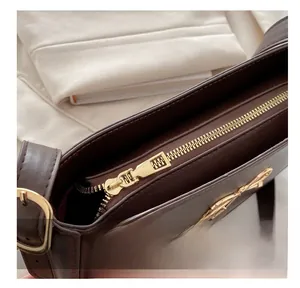 Detailed macro view of the gold bow hardware and metal zipper on brown leather handbag