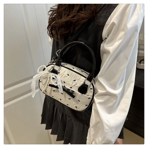 Detail of white pleated bag with black leather handles and oversized lace pearl bow