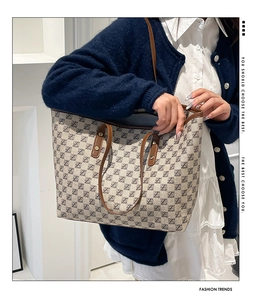 Detailed close-up of a beige tote bag with a repeating monogram pattern and brown leather straps