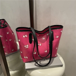 Pink tote bag with cherry print and black shoulder straps on a white stool decor