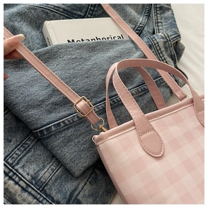 Detailed view of pink plaid crossbody bag with golden hardware on denim background