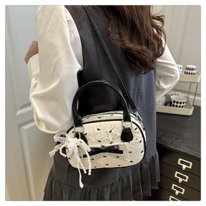 Close-up of white pleated crossbody bag with black bow prints and lace pearl charm