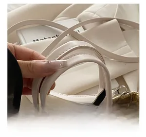 Detail shot of the woven straw handbag featuring a white leather handle and metal D-ring