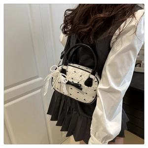 Detail of white wrinkled bag with black bow prints and lace pearl charm on a model