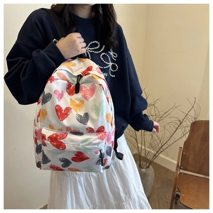 Detail of white backpack with colorful heart print and front zipper on a female model