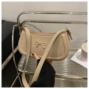 Detail of cream-colored shoulder bag featuring a decorative golden metal bow and smooth finish