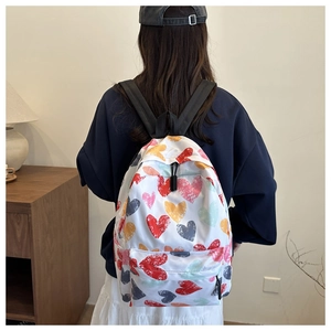 Detail of white nylon backpack featuring colorful heart patterns and dual zipper design