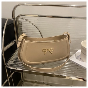 Detailed shot of beige baguette shoulder bag with gold bow clasp on acrylic stand