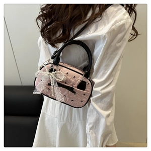 Detail of pink jacquard crossbody bag with lace bow and elegant pearl charm on model