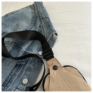 Detailed close-up of khaki nylon chest bag fabric and black strap over a denim jacket