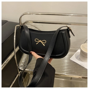 Detail of black faux leather shoulder bag with gold bow clasp in a hand-held setting