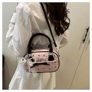 Close-up of pink textured handbag with black bow embroidery and pearl lace charm