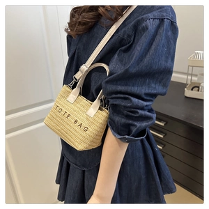 Close-up of straw tote bag with TOTE BAG text and adjustable leather shoulder strap