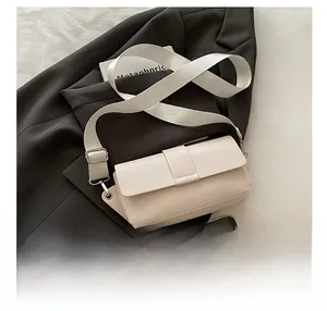 Detail view of a cream crossbody bag with wide strap on a stylish black blazer background