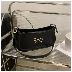 Detail of black underarm bag with gold bow clasp on a modern shelf with accessories