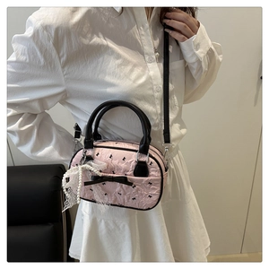 Pink quilted crossbody bag with black bow and elegant lace pearl details on a model