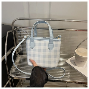 Detail of light blue gingham bucket bag with leather handles on a modern metal chair