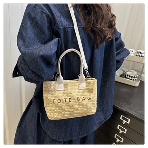 Detail of woven straw tote bag with shoulder strap worn by a model in denim dress