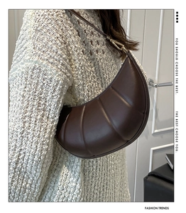 Close-up of a dark brown quilted crescent bag with gold hardware on a model