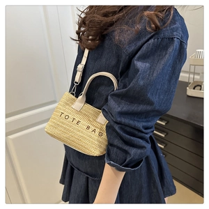 Detail of straw woven tote bag with adjustable leather shoulder strap and black text
