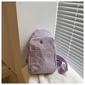 Detail showing lilac nylon crossbody bag with metallic logo on a soft striped cushion