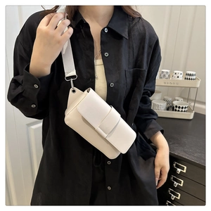 Minimalist beige flap crossbody bag with wide fabric strap shown in an urban setting