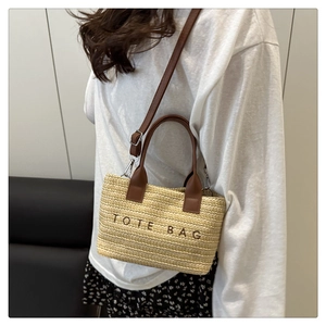 Detail of straw tote bag featuring brown leather handles and black TOTE BAG embroidery