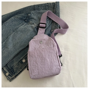 Macro detail of lavender nylon chest bag with pleated texture and metal 'M' logo