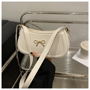 Detailed view of cream leather shoulder bag featuring a golden metal bow decorative buckle