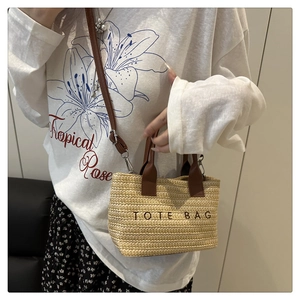 Detail of woven straw tote bag with brown leather handles and TOTE BAG embroidery