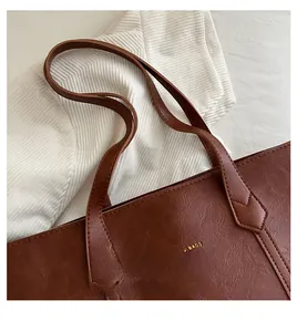 Detail of a brown tote bag featuring golden logo lettering on premium leather material
