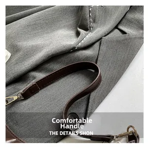 Close-up of grey canvas crescent bag featuring brown faux leather strap and gold metal clasp