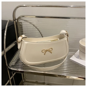 Detail shot of a creamy white underarm bag with a golden bow buckle on a glass cart