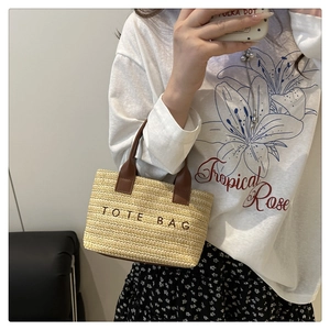Detail of hand-woven straw tote bag featuring brown leather handles and TOTE BAG embroidery