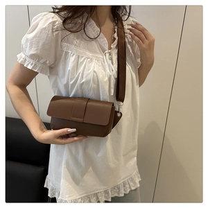 Brown minimalist leather crossbody bag with wide nylon strap worn by a female model
