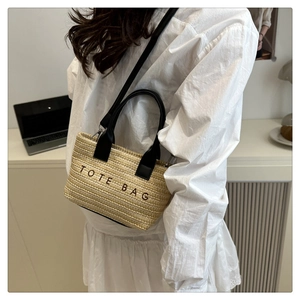 Detail of hand-woven straw tote bag with black handles and adjustable shoulder strap