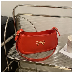 Close-up of red glossy leather shoulder bag with a gold bow metal buckle detail