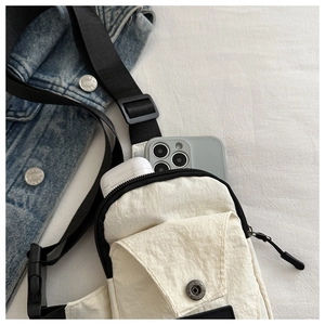 Detail of off-white nylon crossbody bag showing storage for phone and earbuds case