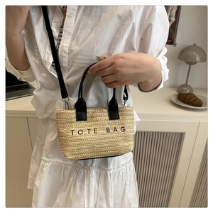Detail of woven straw tote bag featuring black leather handles and embroidered logo
