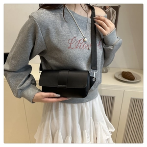Detail of black matte flap crossbody bag with wide shoulder strap worn with casual outfit