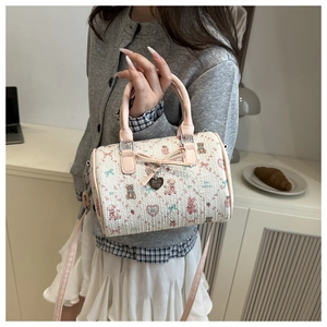 Détail du sac boston beige avec nœud en ruban rose et pendentif en métal en forme de cœur