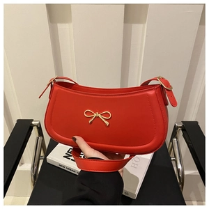 Detail of red leather shoulder bag featuring a prominent gold bow metal buckle clasp