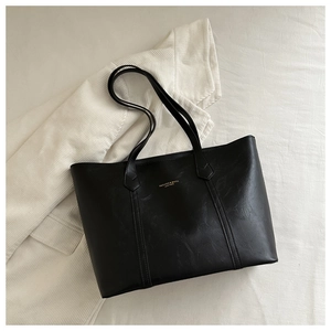 Detail of black leather tote bag with gold lettering on white striped suit background